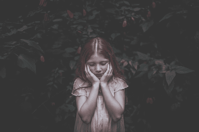 petite fille posant devant un arbre, les mains posées sous ses joues, les yeux fermés.